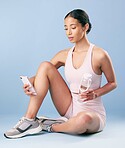 Mixed race fitness woman texting while break from her workout in studio against a blue background. Young hispanic female athlete sending a text message while taking a rest. Health and fitness