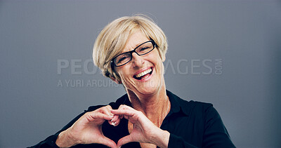 Buy stock photo Heart, studio and portrait of mature woman with gesture for support, kindness and care. Happy, confident and person with emoji, sign and hope for thank you, charity and love on gray background
