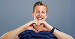 Hands in heart, studio and portrait of man with gesture for support, kindness and care. Happy, confident and person with emoji, sign and hope for thank you, charity and love on blue background
