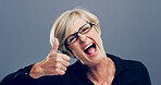 Mature, excited woman and portrait with thumbs up for feedback, opinion or good job on a gray background. Female person, glasses or model with like emoji or yes sign in studio for positive approval