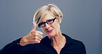 Mature woman, portrait and thumbs up with smile for feedback, opinion or good job on a gray background. Female person, glasses or model with like emoji or yes sign in studio for positive approval