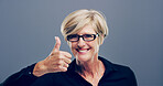 Mature, happy woman and portrait with thumbs up for good job, feedback or opinion on a gray background. Female person, glasses or model with like emoji or yes sign in studio for positive approval