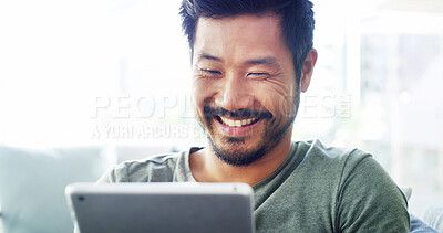 Buy stock photo Tablet, relax and smile with Asian man on sofa for social media, streaming and networking app. Online post, newsletter and update with person in living room at home for chat, comment and contact