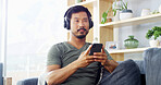 Headphones, man and thinking with phone in home for music choice, streaming service or podcast search. Relax, person or thoughtful with smartphone on sofa for listening to radio app or audio playlist
