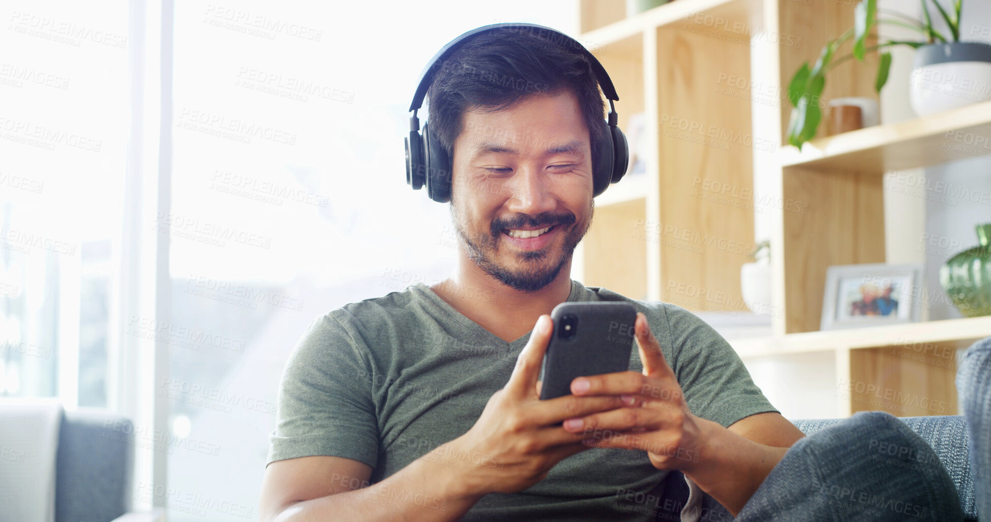 Buy stock photo Headphones, man and typing with phone in home for music search, streaming service and audio playlist. Relax, person and happy with smartphone on sofa for listening to radio app and podcast website