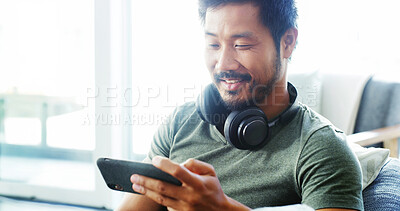 Buy stock photo Phone, smile and relax with Asian man on sofa for streaming service, film app and movies. Happy, media subscription and headphones with person and mobile in living room at home for digital and watch