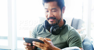 Buy stock photo Phone, happy and relax with Asian man on sofa for streaming service, film app and movies. Smile, media subscription and headphones with person and mobile in living room at home for cinema and series