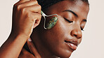 Facial roller, skincare and black woman in studio with natural, health and beauty routine. Wellness, massage and African female person with jade stone tool for lymphatic drainage by white background.