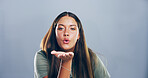 Portrait, woman and blowing kiss with romance for love, affection or greeting on a gray studio background. Creative, female person or model with care, palm or flirt in distance on mockup space