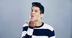 Portrait, man and blowing kiss with flirt for love, affection or greeting on a gray studio background. Creative, male person or model with care, palm or romantic gesture in distance on mockup space