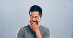Asian man, crazy and laughing in studio for funny joke, lol and smile for comedy. Face, excited and happy person with humor, silly or comic emotion with eyes closed isolated on gray background space