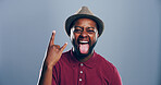 Crazy, happy or portrait of black man with rock hand gesture or tongue out in studio on gray background. Space, edgy rocker and African person with devil horn sign, funky emoji and wild punk symbol