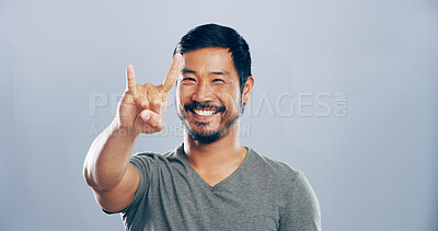 Buy stock photo Rock, emoji and portrait of Asian man in studio with hand gesture for crazy, heavy metal and edgy attitude. Mockup space, happy and person with punk sign, symbol and devil horns on gray background