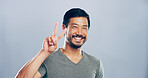 Portrait, space and happy Asian man with peace sign, confidence or positive attitude for mockup. Grey background, creative person and proud male model in studio for cool gesture or v symbol in China