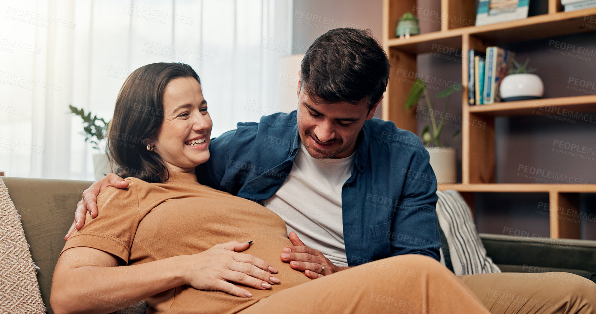 Buy stock photo Pregnant woman, man and touch stomach on sofa, smile or laugh for baby kick, connection and love in house. Couple, parents and hug with care, support and happy with pregnancy for growth with belly