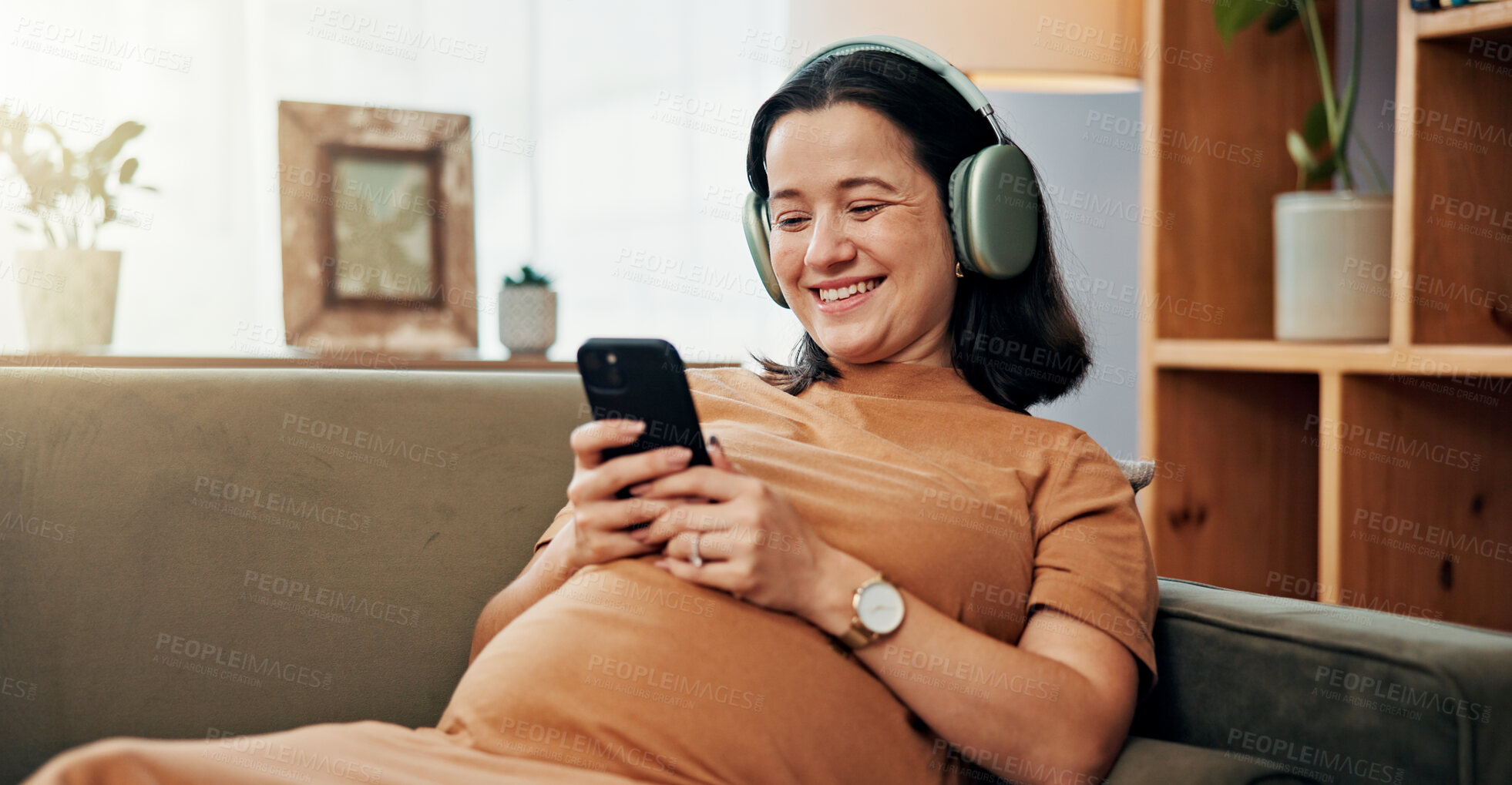 Buy stock photo Pregnant woman, phone and headphones on sofa for smile, texting or search for music on mobile app in home. Person, smartphone and relax with streaming, subscription or video on social media in house