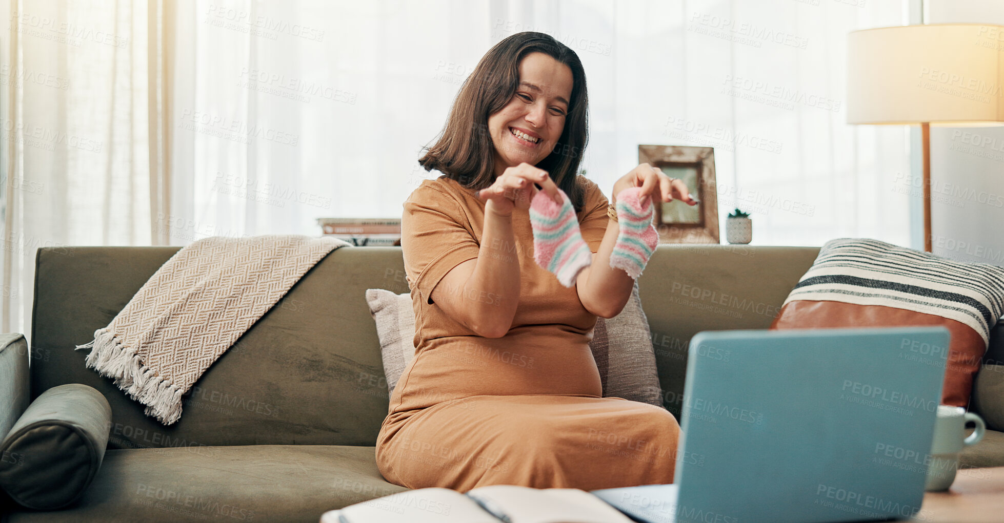 Buy stock photo Pregnant, woman and baby clothes for video call, happy and sharing motherhood on social media with laptop. House, virtual chat and socks for gender reveal, communication or preparation for child