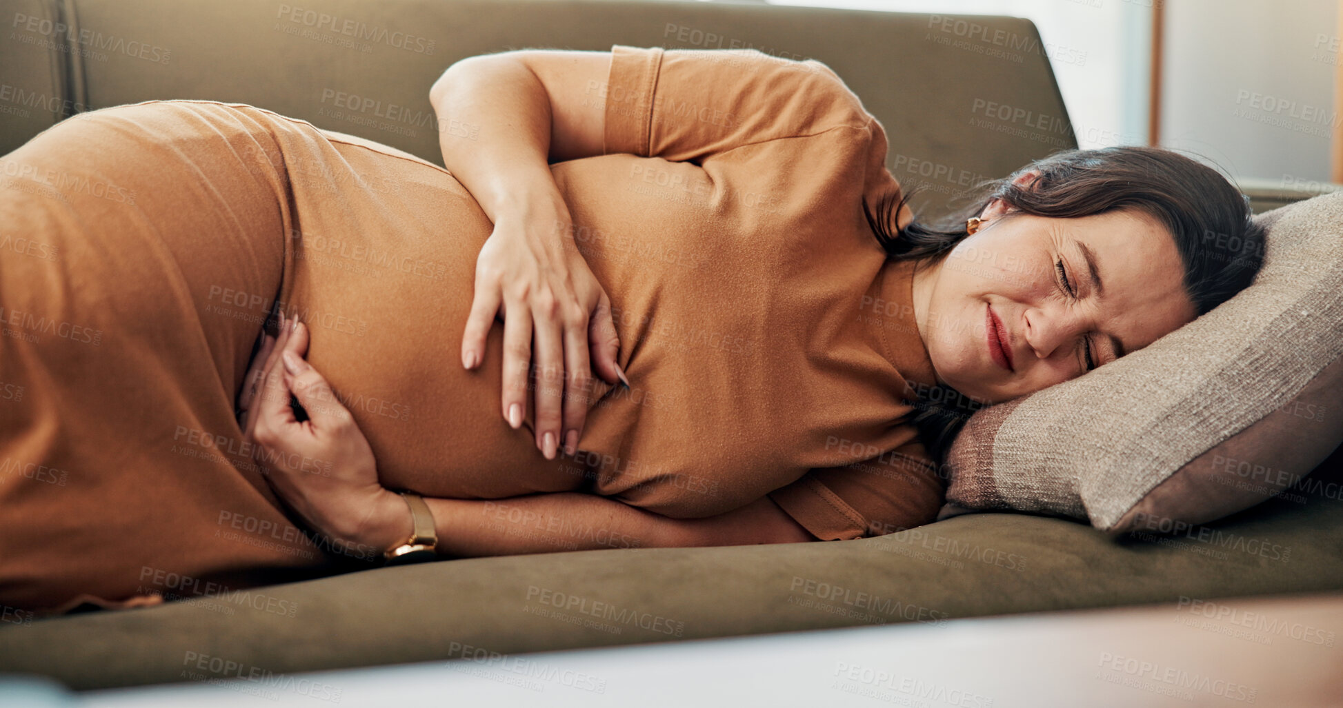 Buy stock photo Home, pregnancy and woman on sofa with pain, cramps and contractions for resting in living room. Parenting, maternity health and pregnant person on couch with discomfort, prenatal stress and hurt