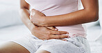 Woman, hands and sickness in bed with stomach pain, menstruation cramps and IBS symptoms. Girl, discomfort and health risk in home bedroom with tummy ache, endometriosis and warm compress for relief