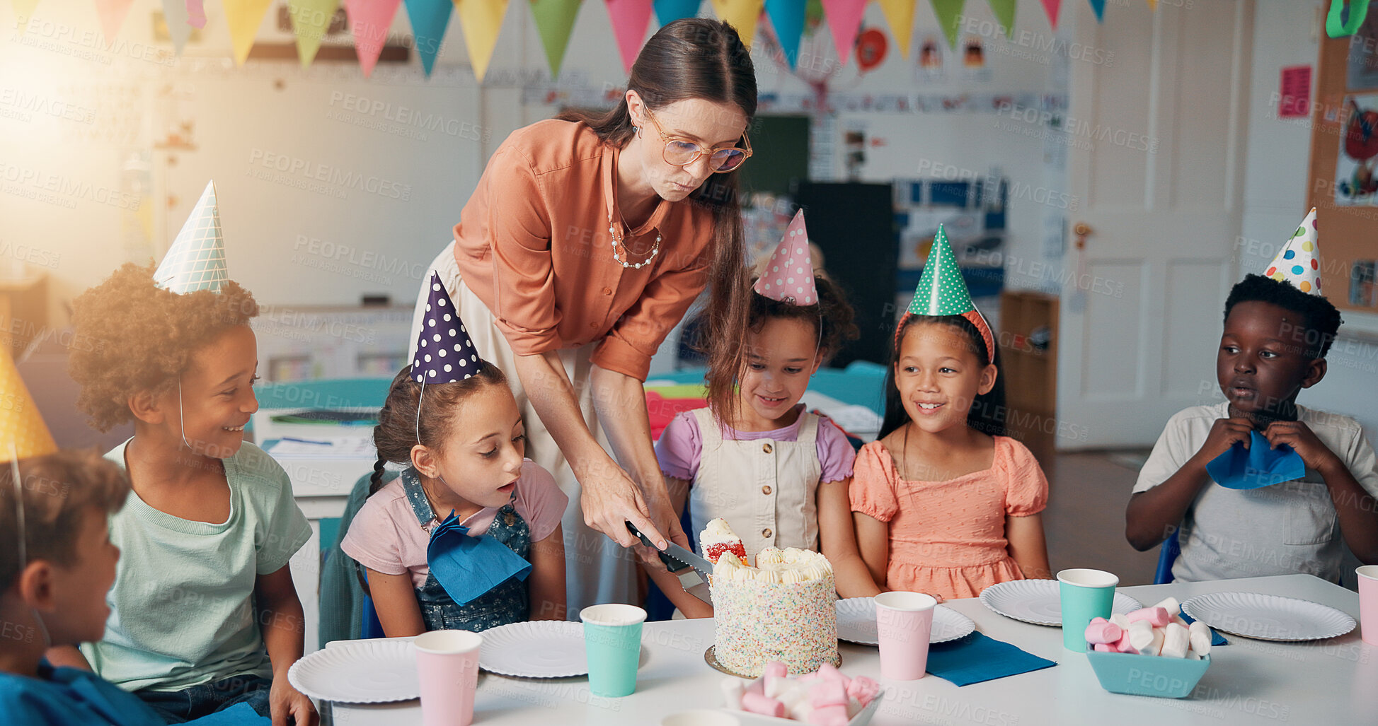 Buy stock photo Birthday, cutting and teacher with cake for children in classroom for group party with dessert, hats and decoration. Happy, eating and woman educator with students for celebration of special event.