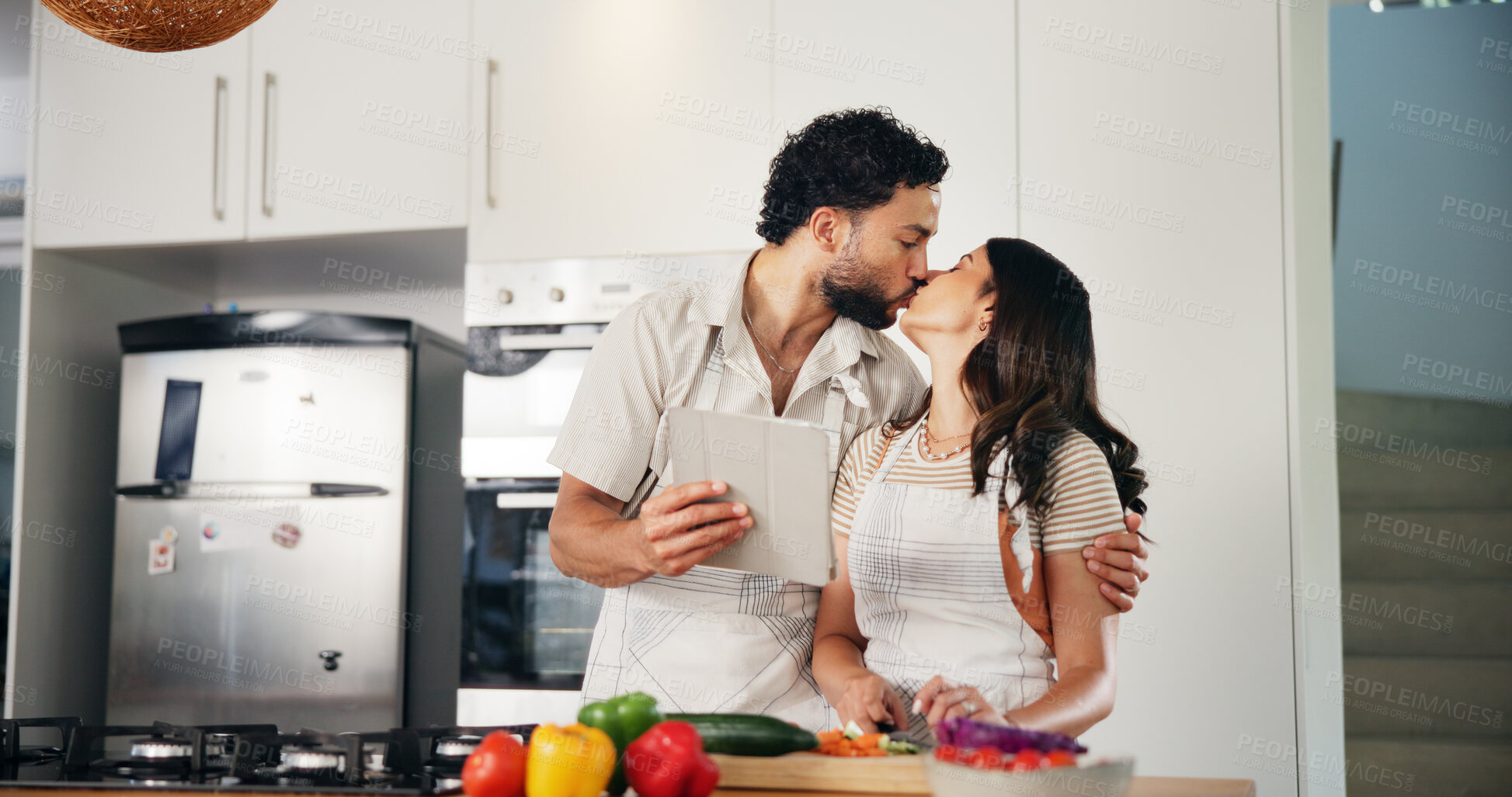Buy stock photo Tablet, kiss and cooking with couple in kitchen for health, food and online recipe. Love, bonding and nutrition ingredients with man and woman helping at home for meal prep, wellness and lunch menu