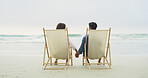 Couple, beach chair and holding hands on vacation for honeymoon, holiday or bonding outdoor. Woman, man and relationship by sea for space, romantic date and care with security in commitment 