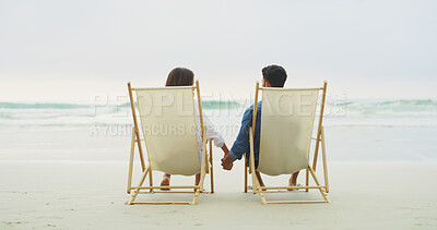 Buy stock photo Couple, beach chair and holding hands on vacation for honeymoon, holiday or bonding outdoor. Woman, man and relationship together at sea for space, romantic date and care with security in commitment
