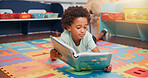 African boy, book and floor in classroom for development, storytelling and knowledge at academy. Child, learning and study on mat for scholarship, reading and info with course at elementary school