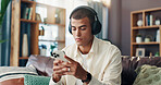 Man, texting and phone with headphones on sofa for music, sound and streaming subscription in living room. Person, scroll and smartphone with social media, mobile app and chat on couch at apartment
