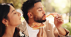 Couple, picnic and eating pizza at park together for romantic date, lunch and bonding for relationship. Man, woman and share fast food outdoor, hungry or enjoy takeaway to relax with partner for love
