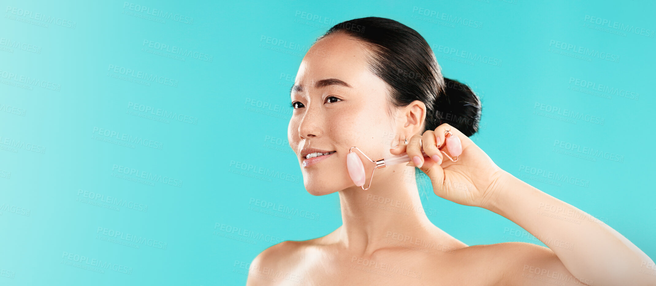 Buy stock photo Beauty, woman or rose quartz roller in studio for lymphatic drainage, puffiness reduction or self care routine. Mockup space, Asian person or happy with cosmetics tool for skincare on blue background