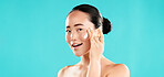 Studio, portrait and asian woman with cream for skincare, wellness and anti aging benefits with smile. Mockup, female person and apply with cosmetics for beauty, face moisturizer and blue background