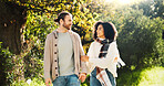 Outdoor, holding hands and couple on walk, talking and people with smile on date, romance or break. Park, man and woman in relationship, bonding and happy for interracial marriage, travel or together