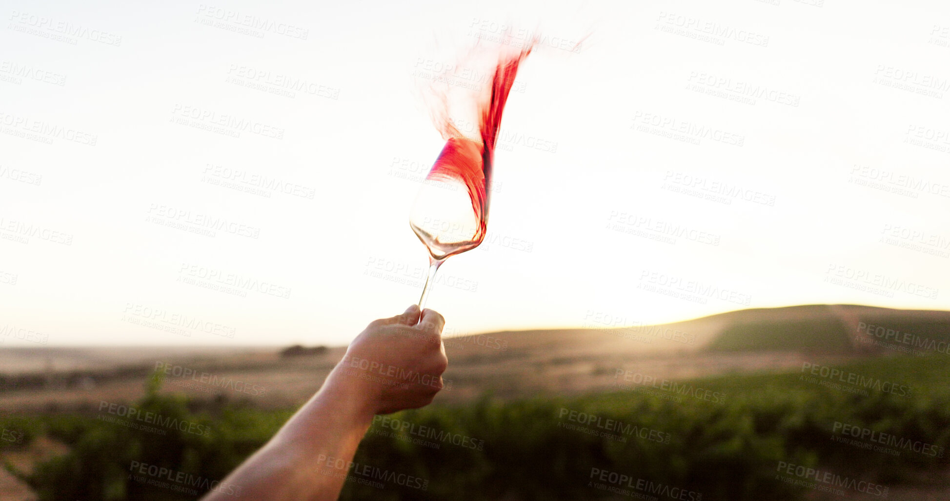 Buy stock photo Hand, red wine and person splash with glass at vineyard, luxury drink and farm or countryside. Winery, tourist and tasting alcohol outdoor or swirl beverage with mockup space at sunset in nature