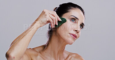 Buy stock photo Beauty, facial massage and thinking with woman in studio for antiaging cosmetics or dermatology. Gua sha, jade and skincare with thoughtful person on gray background for crystal stone face treatment