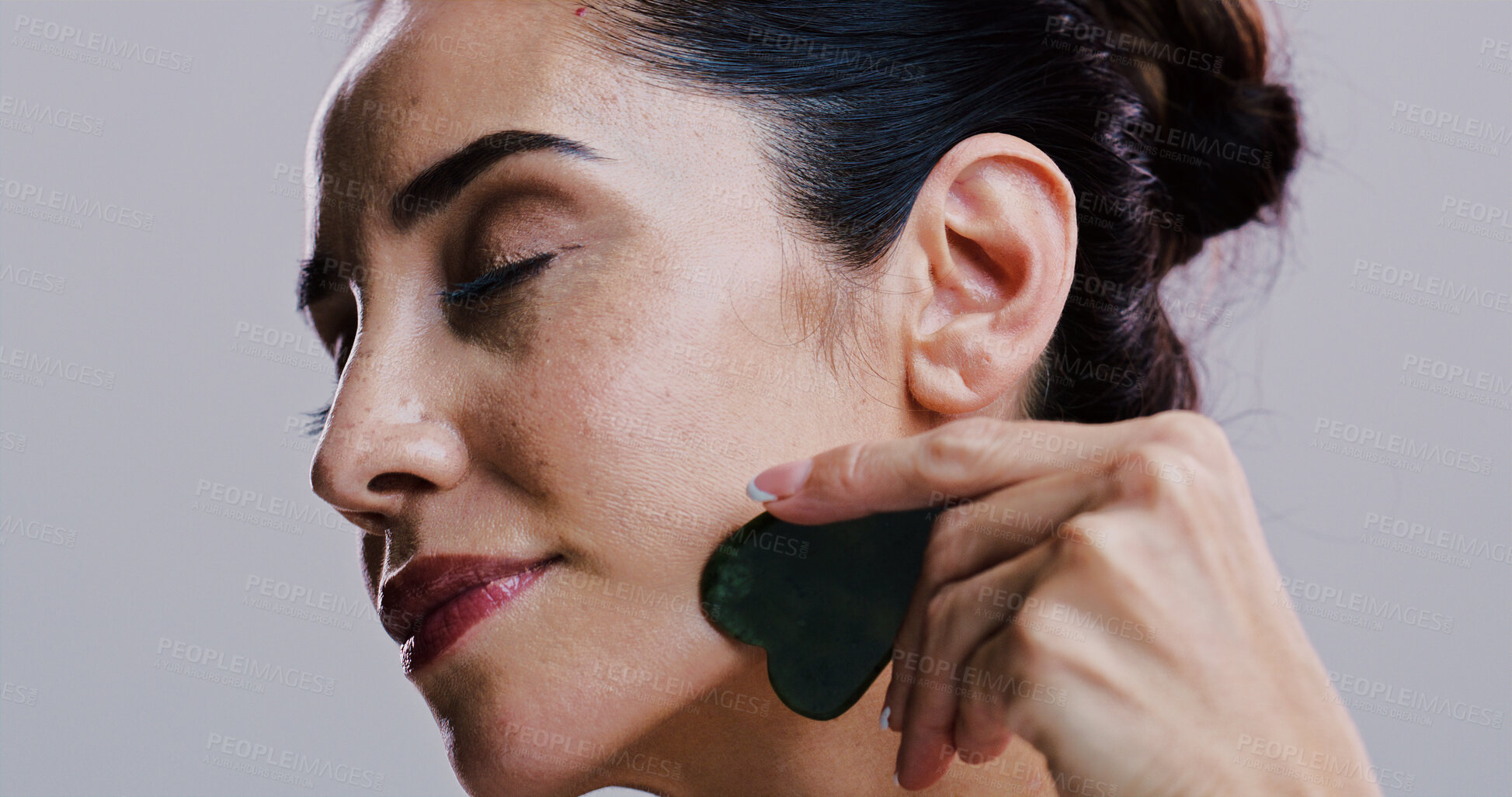 Buy stock photo Beauty, facial massage and stone of woman in studio for antiaging cosmetics or dermatology. Gua sha, natural product and skincare with person isolated on gray background for crystal face treatment