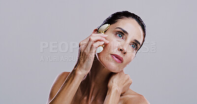 Buy stock photo Beauty, derma roller and thinking of woman in studio for antiaging cosmetics or dermatology. Gua sha, massage and skincare with thoughtful person on gray background for crystal stone face treatment