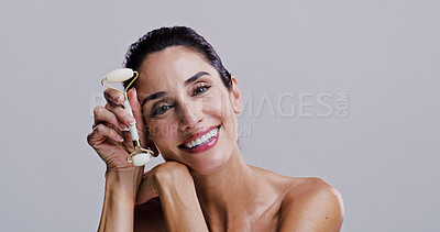 Buy stock photo Roller, portrait and smile of woman in studio for antiaging cosmetics or dermatology. Beauty, massage and skincare with happy person isolated on gray background for crystal stone face treatment