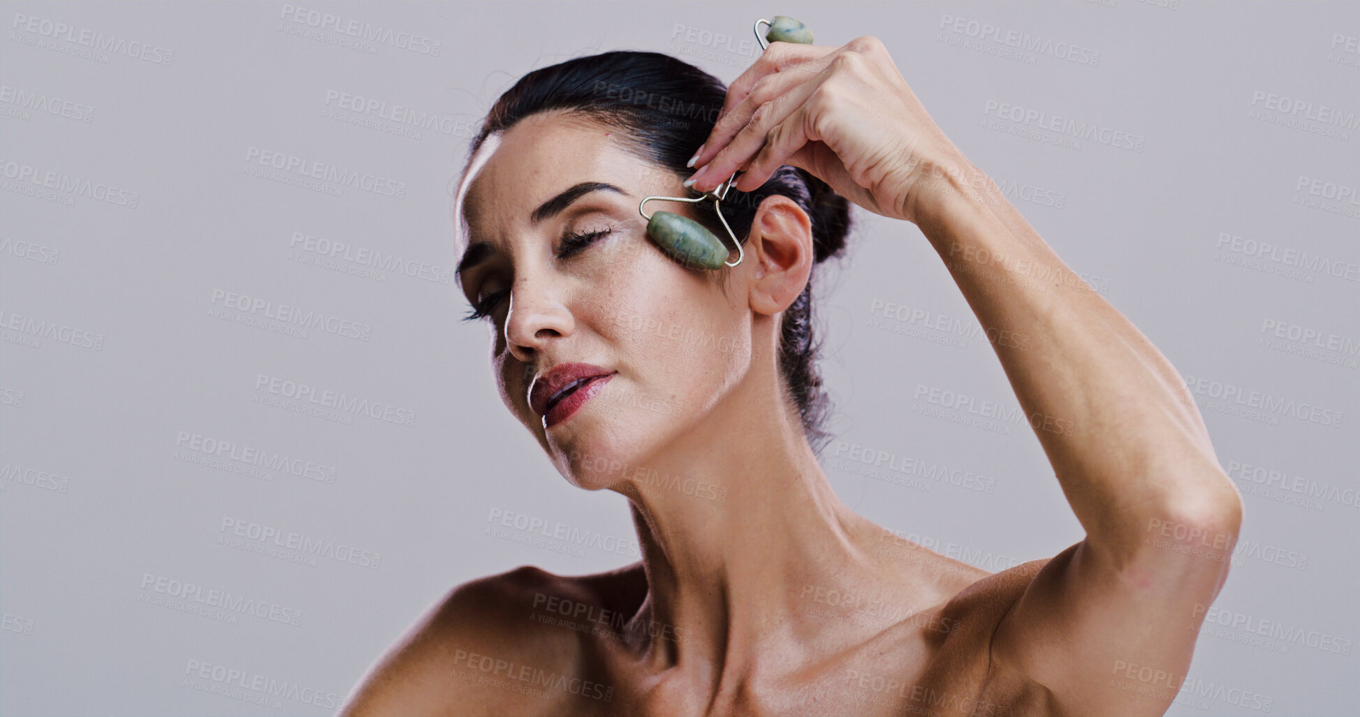 Buy stock photo Beauty, facial and jade roller with woman in studio for antiaging cosmetics or dermatology. Gua sha, massage tool and skincare with person isolated on gray background for crystal stone face treatment