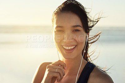 Buy stock photo Happy woman, portrait and earphones on beach for fitness, self affirmation audio and windy at sunset. Athlete, smile and tech at Colombia ocean for workout music, local radio and motivation podcast