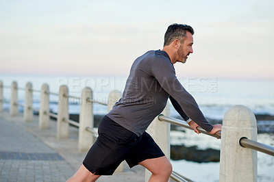 Buy stock photo Mature man, runner and stretching, promenade and ocean with warm up for legs, health and fitness in morning. Person, outdoor and start routine for exercise, training and profile by sea in Italy