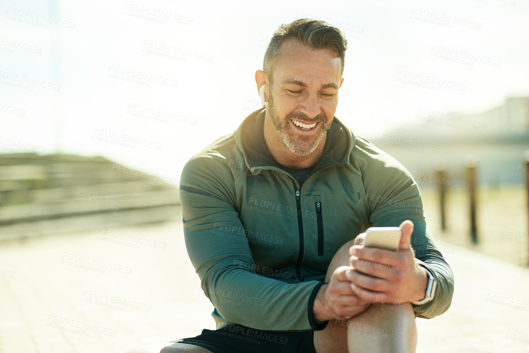 Buy stock photo Man, happy and outdoor with phone for fitness, music and wellness tracking app for care. Mature athlete, mobile and smile in Portugal for streaming service, favorite playlist and warm up tutorial