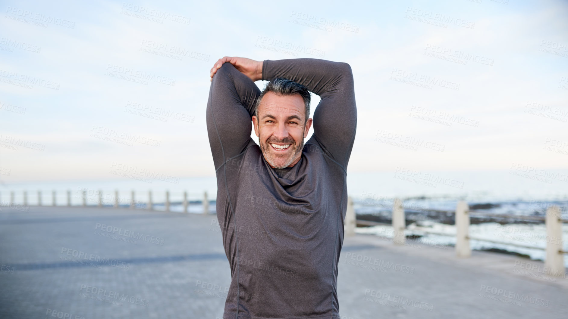 Buy stock photo Happy, mature man and stretching by beach to start, getting ready and muscle preparation outdoor. Athlete, arms warm up and smile at promenade for cardio, wellness challenge and exercise performance