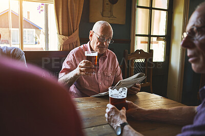Buy stock photo Senior man sitting with friends and drinking beer while reading a newspaper in a pub, elderly man browsing newspaper, drinking a pint of beer