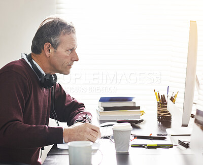 Buy stock photo A businessman using a computer and writing a note in a modern office. A mature male executive working online for business at his desk
