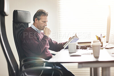 Buy stock photo A businessman reading g book and using a computer in a modern office. A mature male executive working online and doing business research at his desk