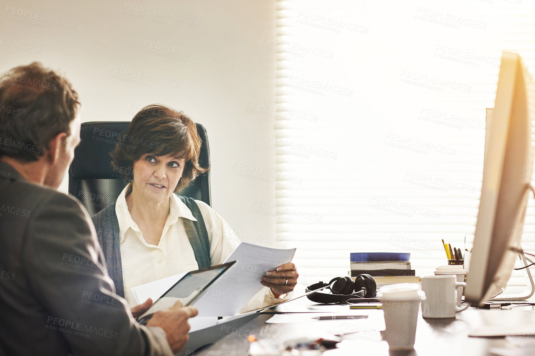 Buy stock photo Two colleagues using a tablet in a modern office. A mature businessman and businesswoman working online with a touchscreen, talking about business matters