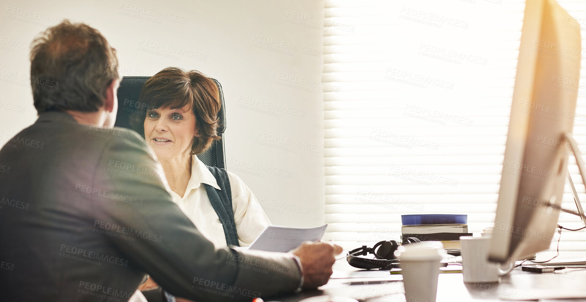 Buy stock photo Two colleagues talking finance in a modern office. A mature businessman and businesswoman working with paperwork, discussing business matters