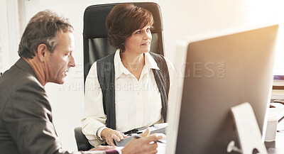 Buy stock photo Two colleagues using a computer in a modern office. A mature businessman and businesswoman working online, talking about business matters