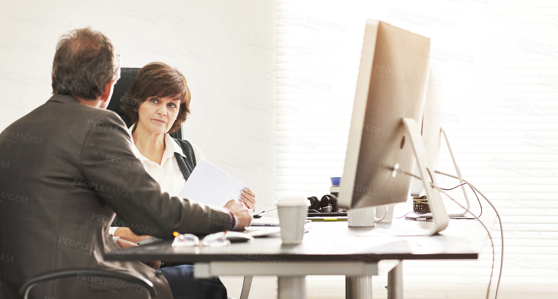 Buy stock photo Two colleagues talking finance in a modern office. A mature businessman and businesswoman working with paperwork, discussing business matters